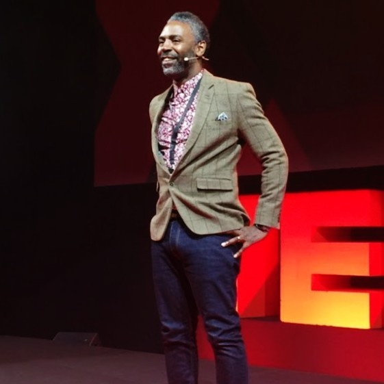 A man, Derek Bruce, stands with hands on hips at a TedX Talk.