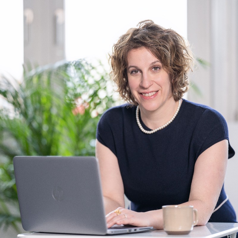 Gorana Sandric, with curly hair and sat at a laptop, sits and smiles at the camera