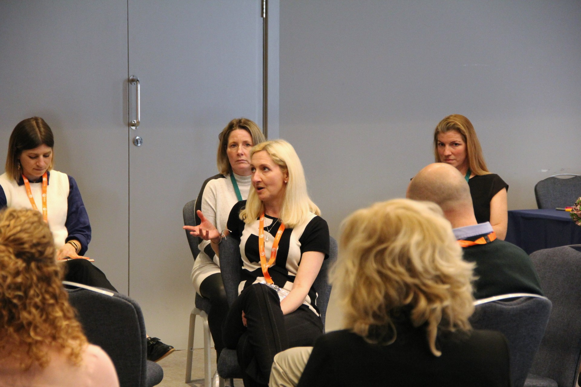 A woman, seated, asks a question of other executives, who are sat around her in a circle
