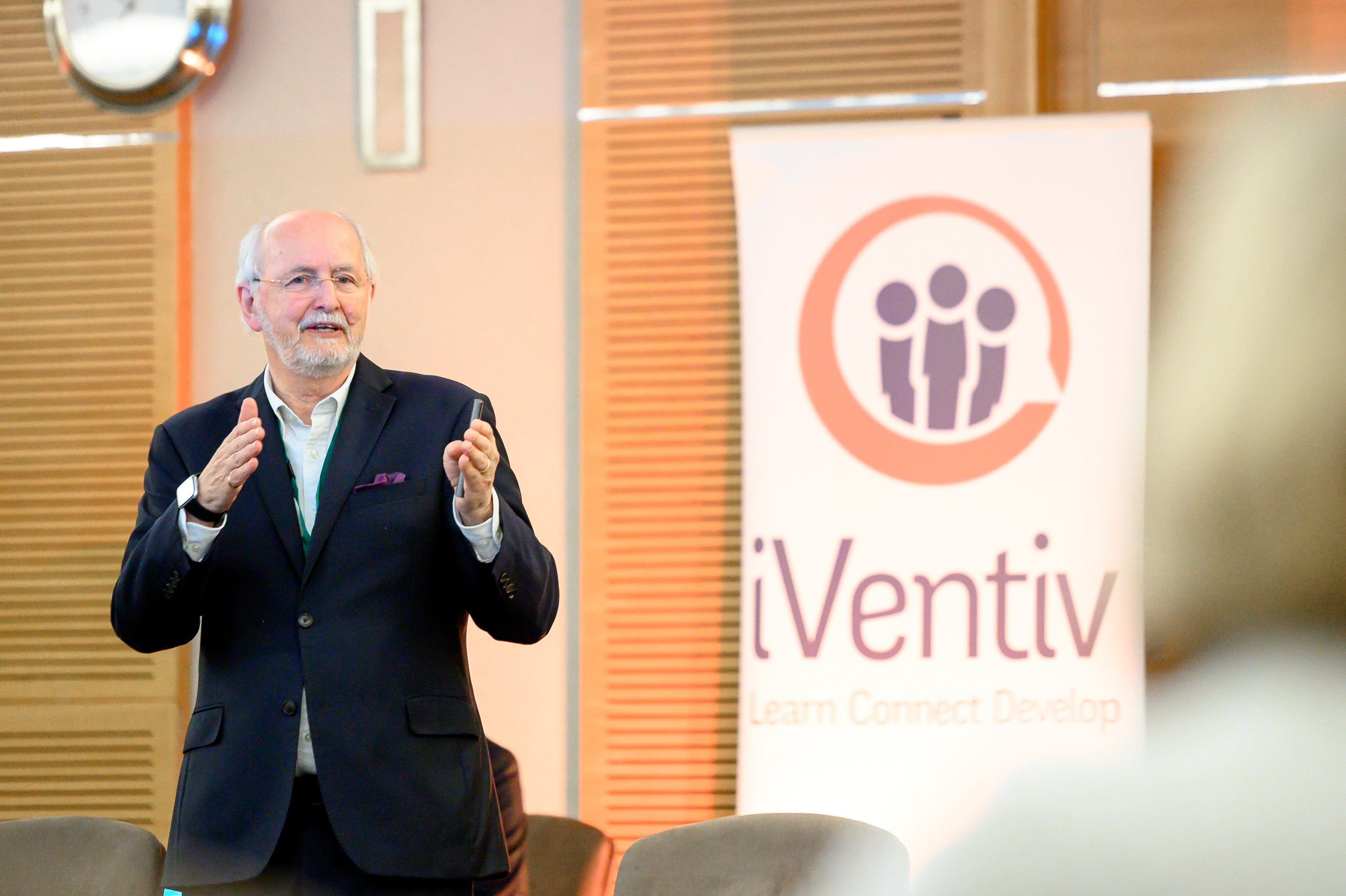 A man, charles jennings, speaks to a group of executives in front of an iventiv banner